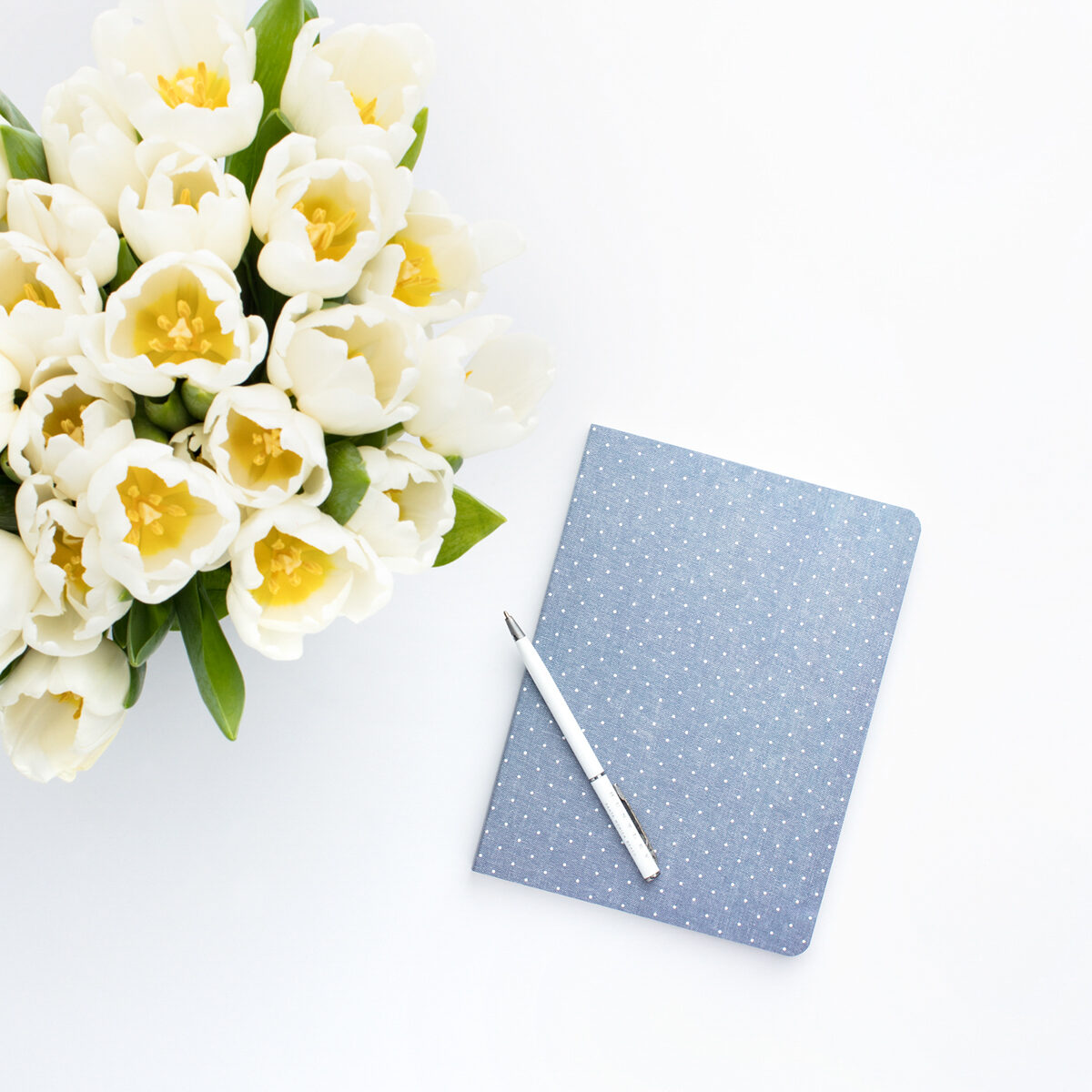 light blue notebook with a pen resting on top and a vase of white flowers to the side.