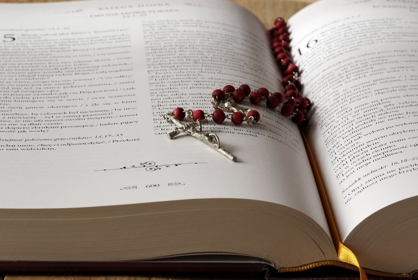 bible open with a rose colored rosary on top 