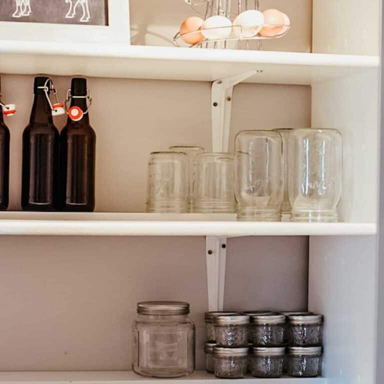 shelving in farmhouse pantry with empty mason jars and glass bottles