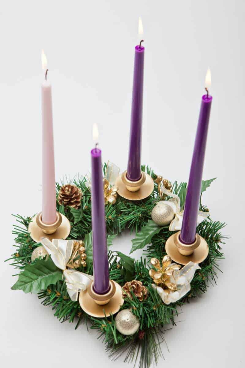 catholic advent wreath on a white table with purple and pink candles lit