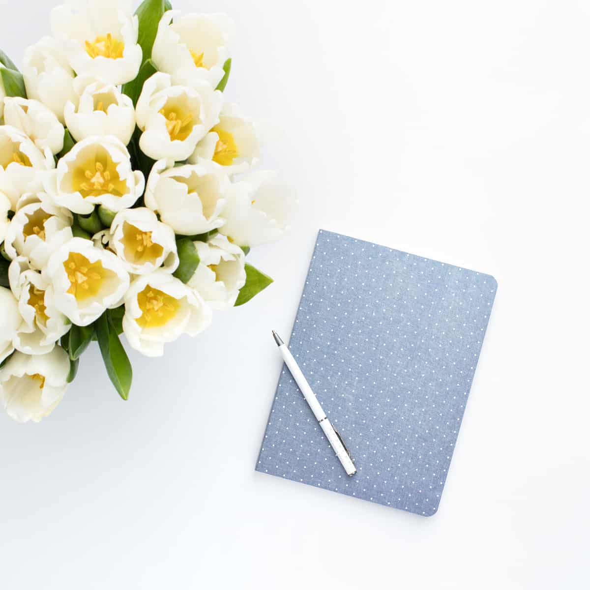 vase with white flowers and blue journal and white pen on top.