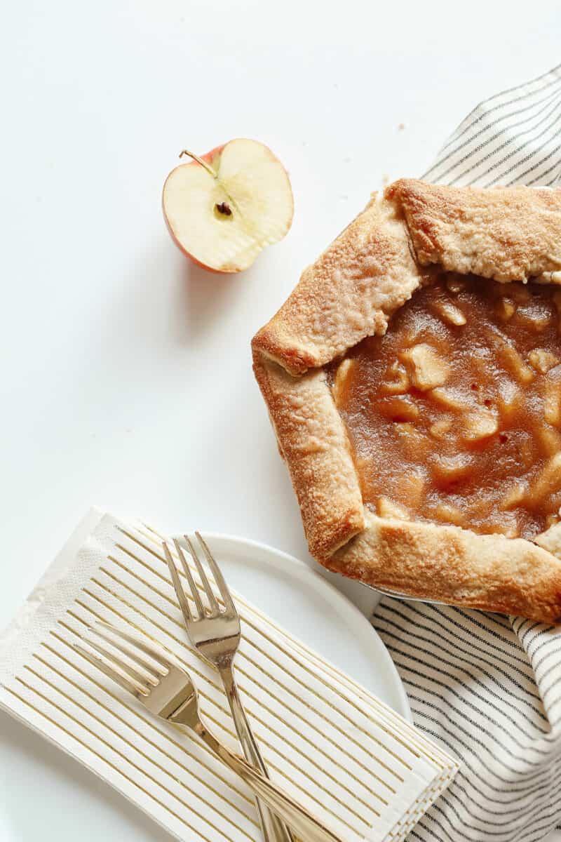 apple tart with a stack of white plates and linens to the side.