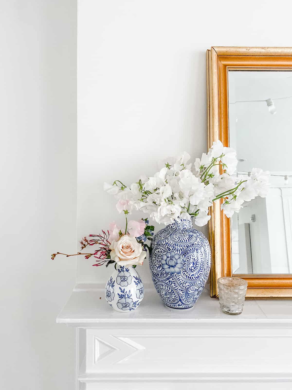small vases of flowers next to a mirror on a shelf. 