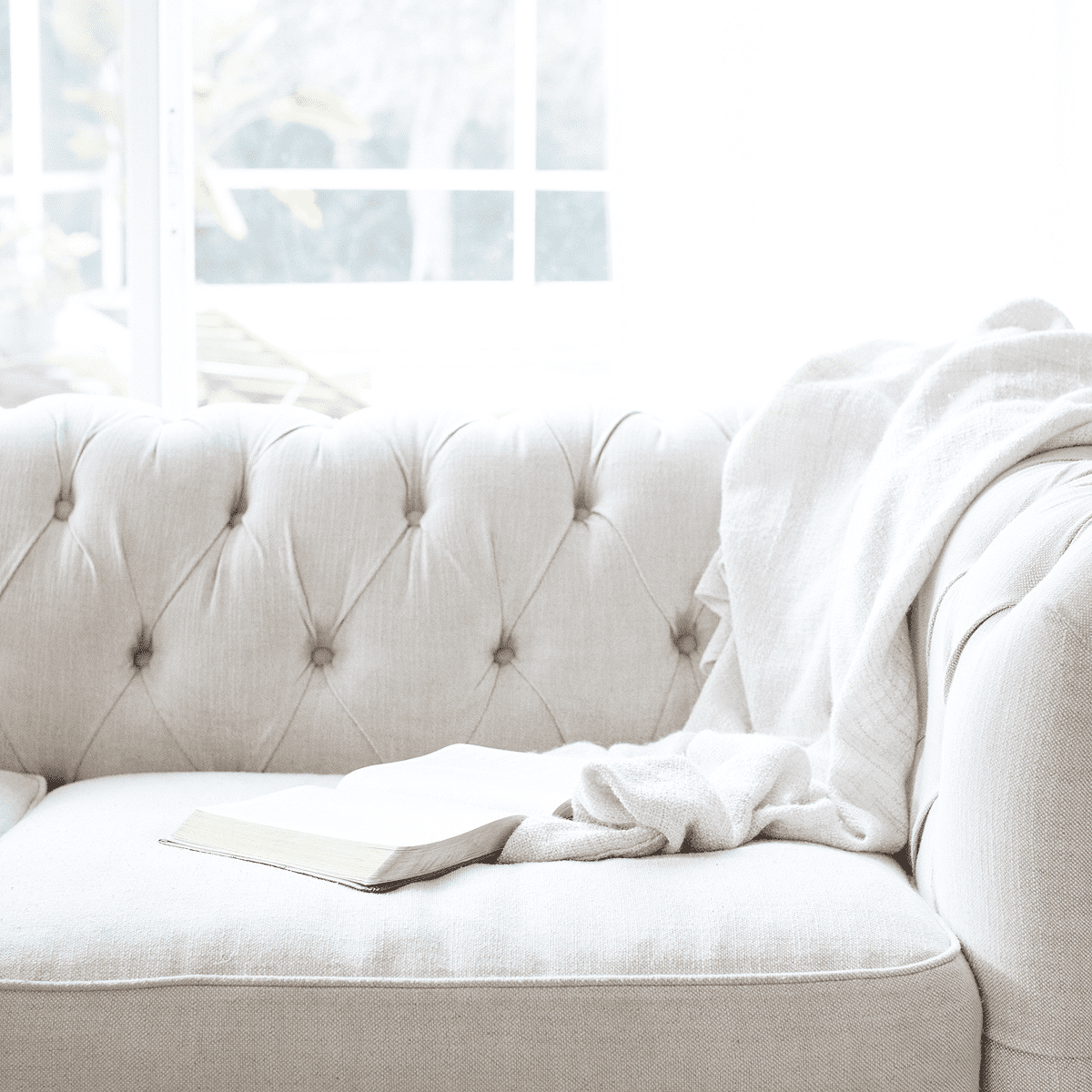 light gray couch with a white throw blanket and open bible on top.