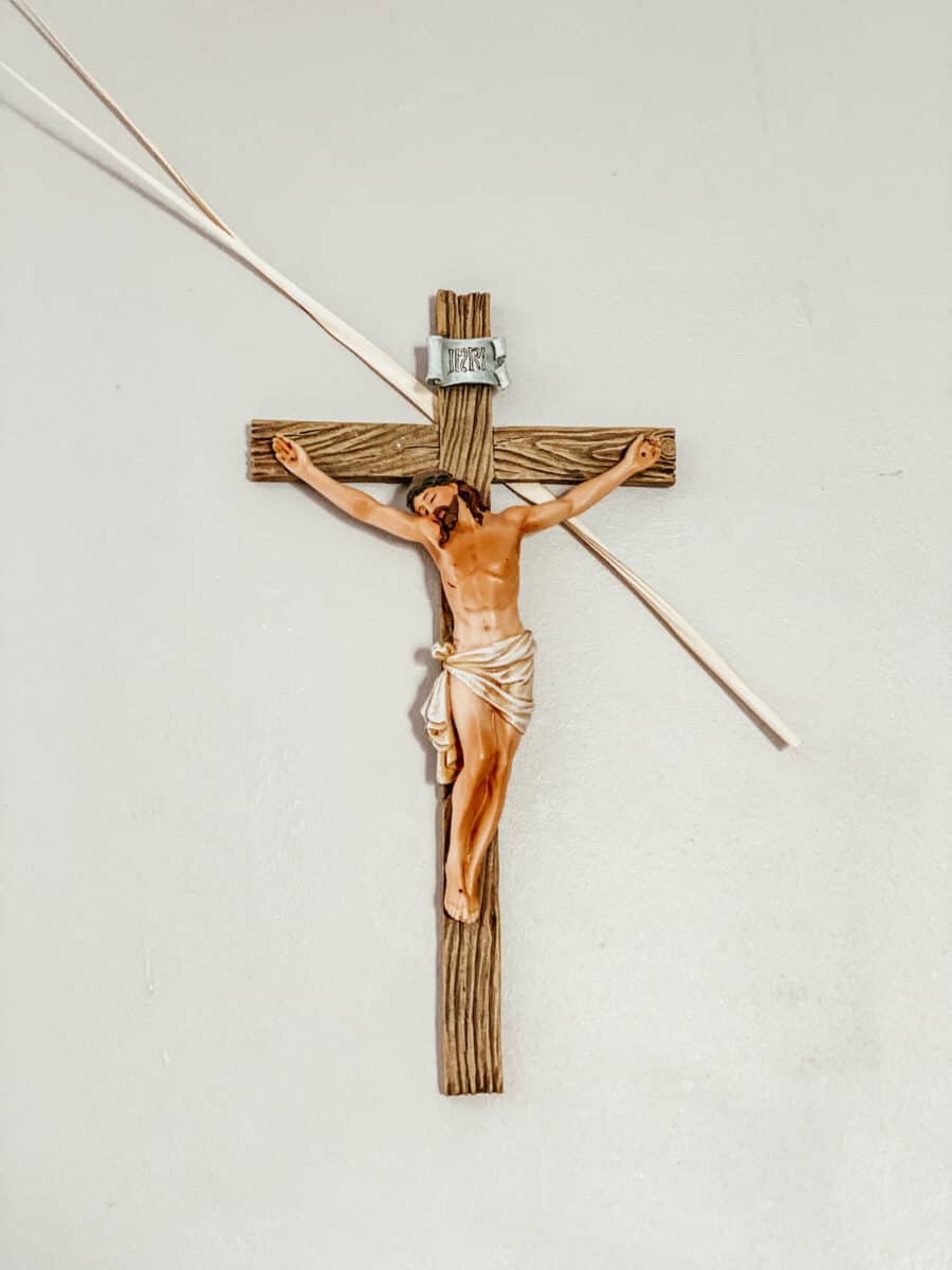 crucifix hanging on the wall with blessed palms behind it.