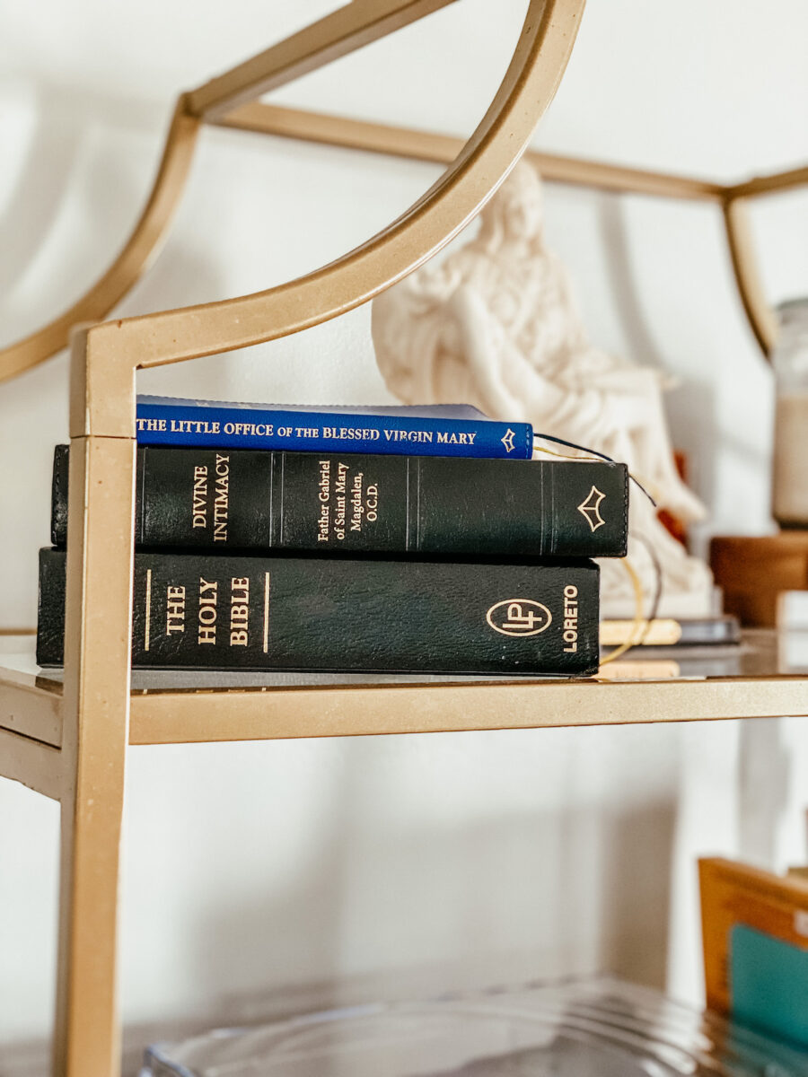 holy bible, divine intimacy, and little office prayer books stacked on a bookshelf.