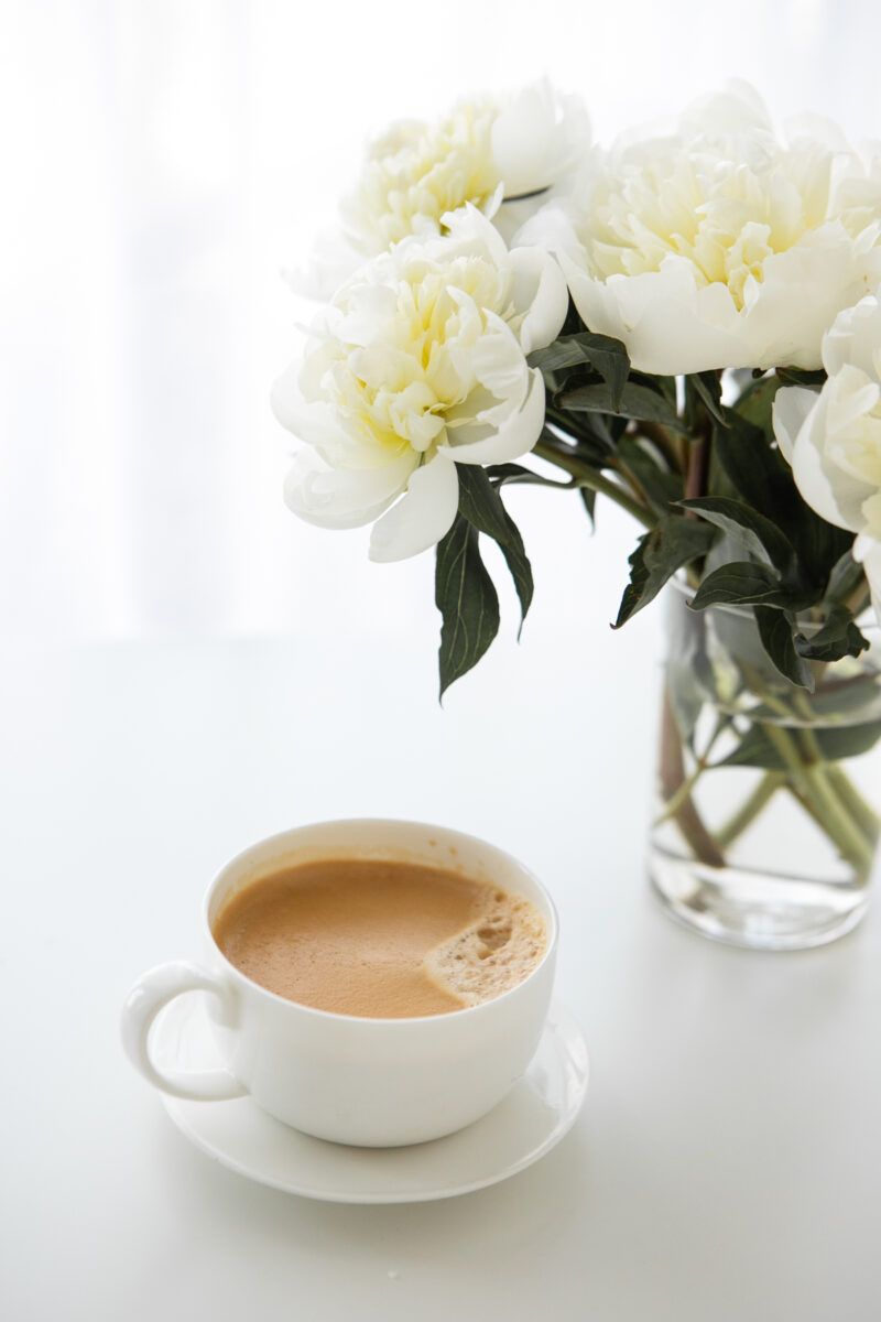 coffee and glass vase with white flowers on a table.