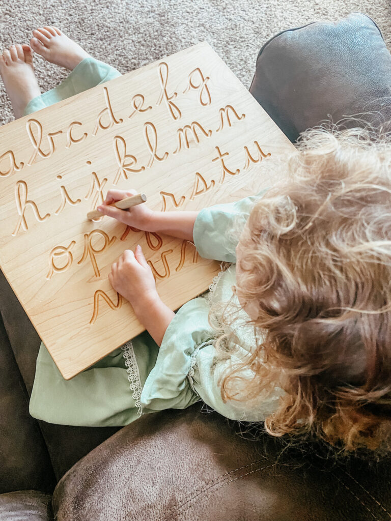 little girl tracing letters on a wooden board.
