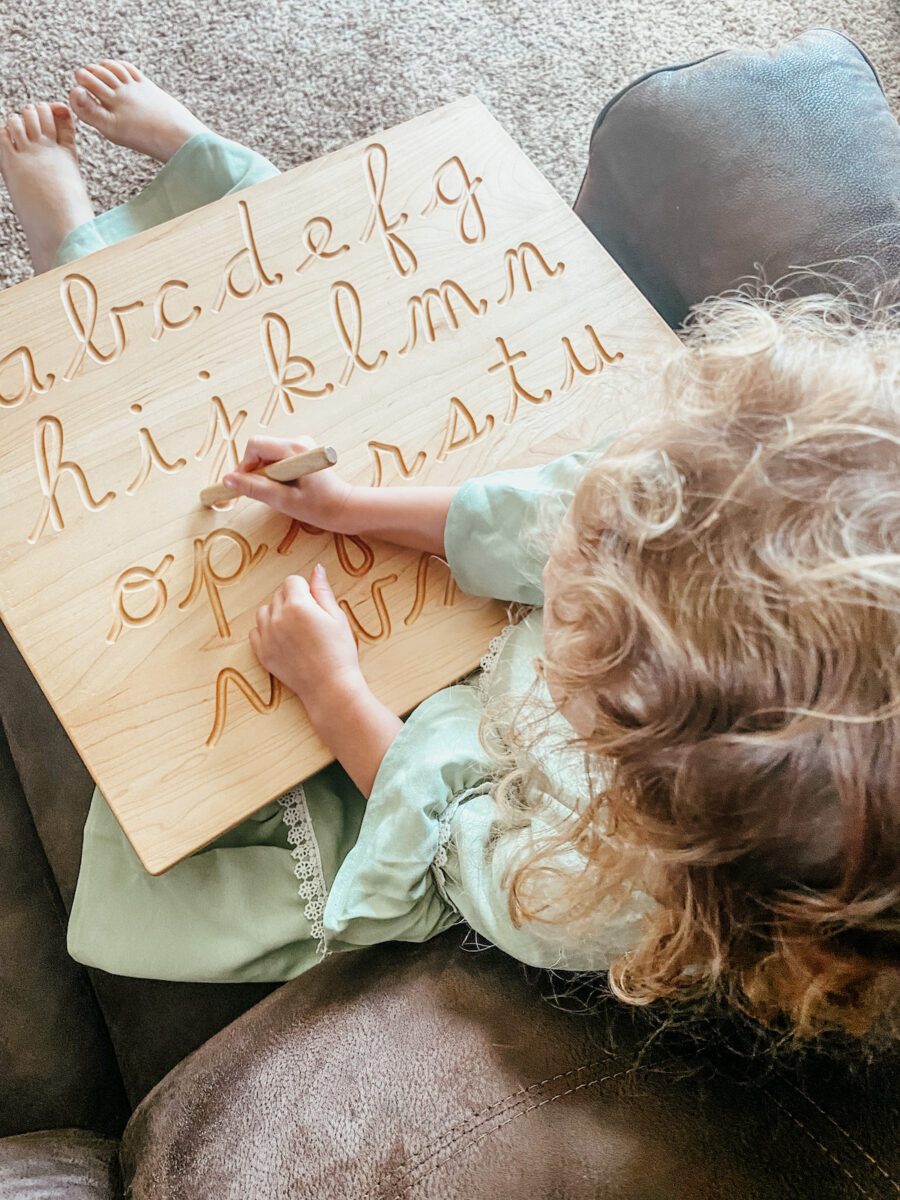 little girl tracing letters on a wooden board. 