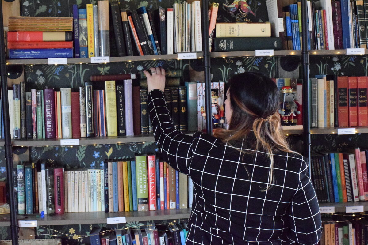 Mary standing in front of the library pulling a book off of the bookshelf.