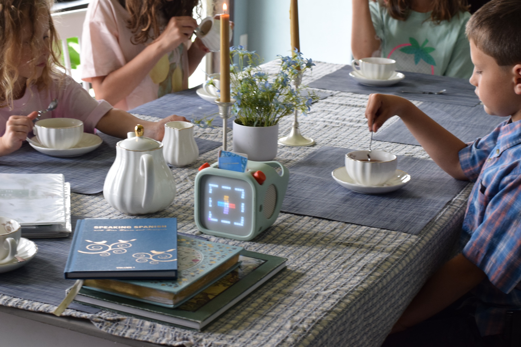 children sitting at a dining table with tea cups and listening to a lesson.