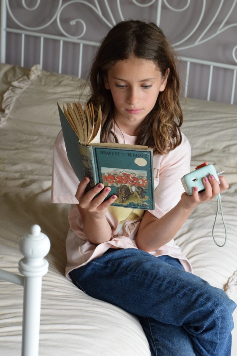 girl reading on a bed while holding a Yoto Player. 