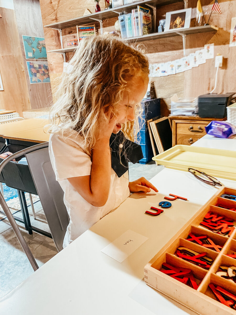little girl building words with wooden letters at a table. 