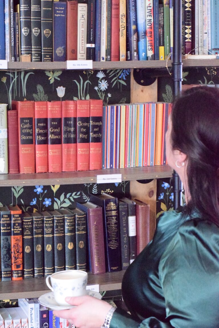 Mary standing in front of the home library with a cup of coffee.